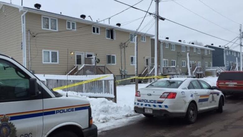 Police vehicles outside a row of two-storey buildings surrounded by yellow crime scene tape.