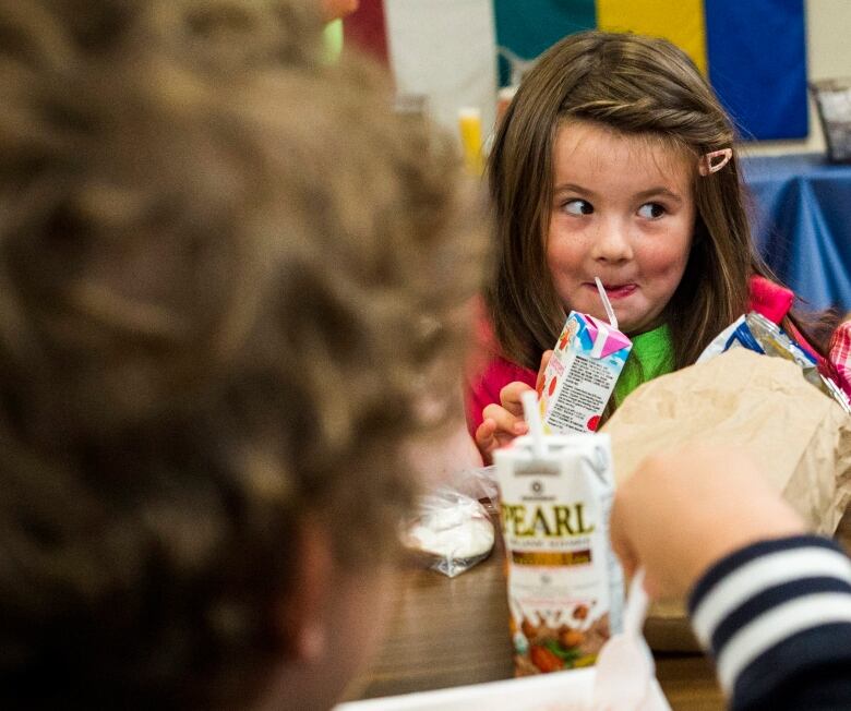 Two young girls smile as they eat a lunch and drink from juice boxes.