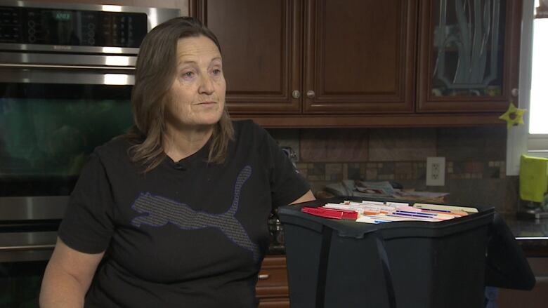 A woman sits beside a bin of files.