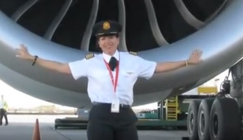 A woman leans on the thrusters of a flight while wearing a pilot's uniform.