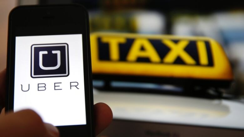 An Uber logo on a smartphone next to a taxi sign on top of a cab.