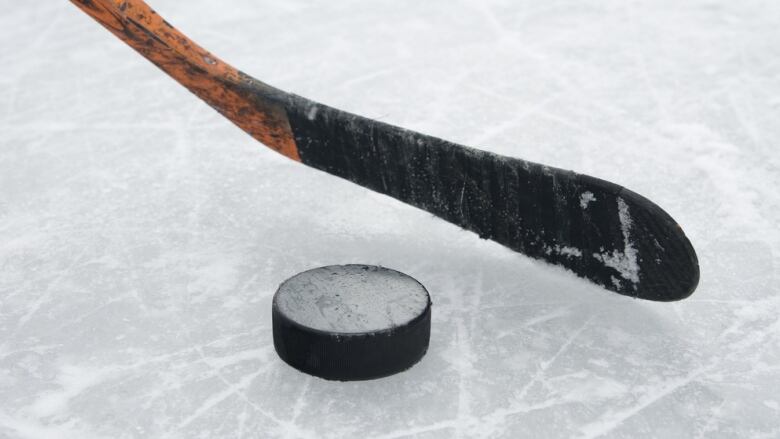 A hockey stick and puck is seen on ice.