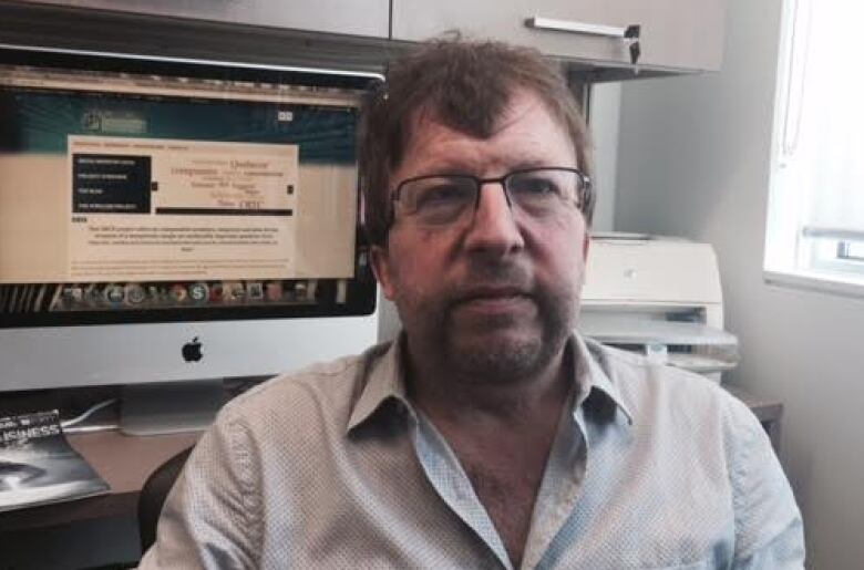 A man with brown hair and a beard wears glasses.