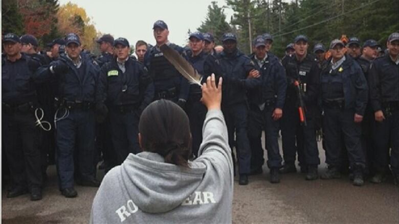 An Indigenous woman holds up an eagle feather in front of a wall of police. 