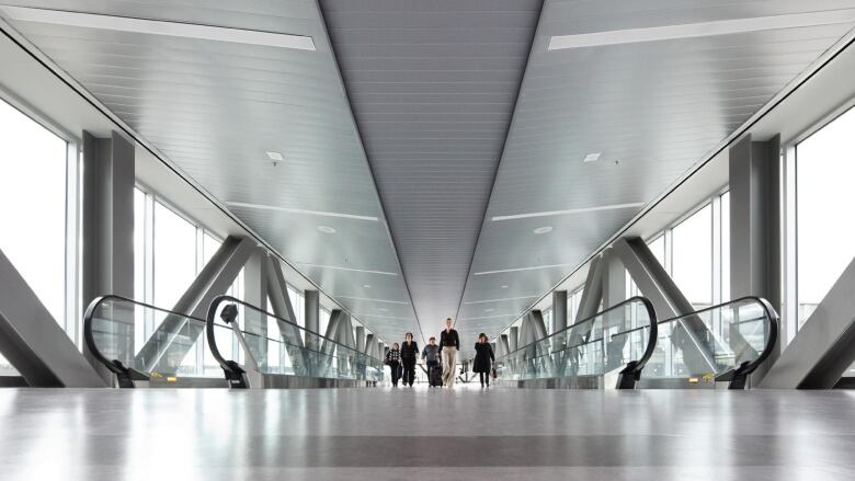 People walk along a grey metal moving walkway at an airport