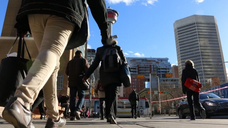 People are walking in downtown Calgary. No faces can be seen and the Calgary tower is in the background