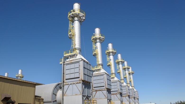 Five large grey and silver steam generators are pictured at an industrial site against a blue sky.