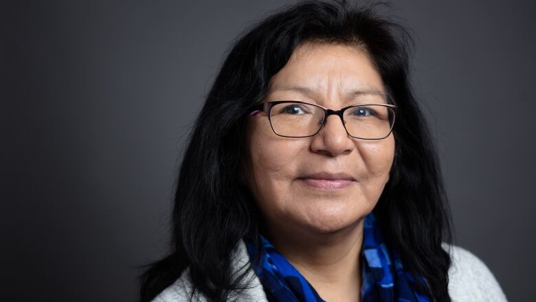 A headshot of a woman with long dark hair, glasses and a blue scarf.