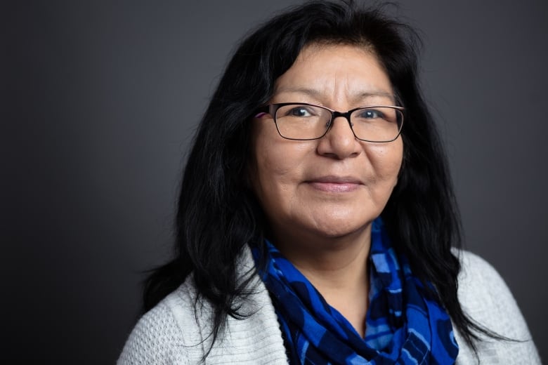 A headshot of a woman with long dark hair, glasses and a blue scarf.