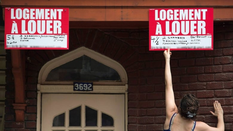 woman taping for rent sign on building