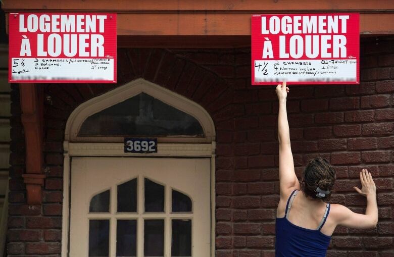 woman taping for rent sign on building