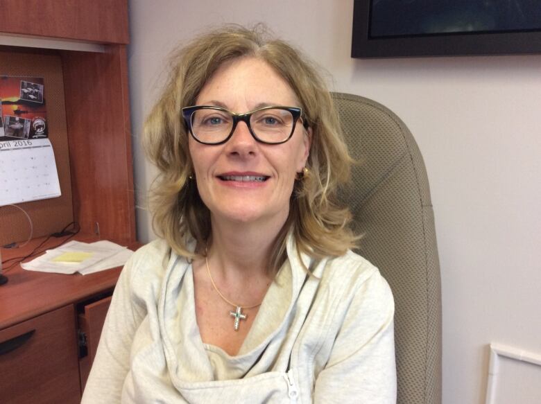 Woman in glasses smiles as she sits at a desk.