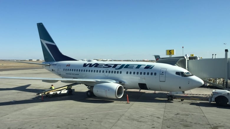 A WestJet plane is parked at a gate at the airport.