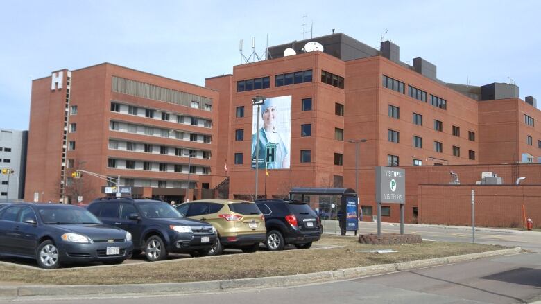 A large red brick building with a large letter 'H' on it, as well as a large image of a health-care provider wearing medical scrubs.