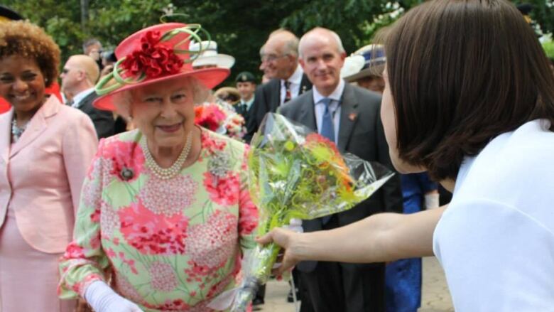 A woman looking away from the camera holds out flowers for Queen Elizabeth.