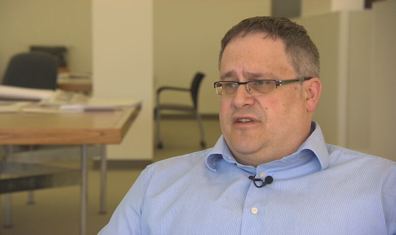 A man wearing glasses and a blue shirt sits in an office.