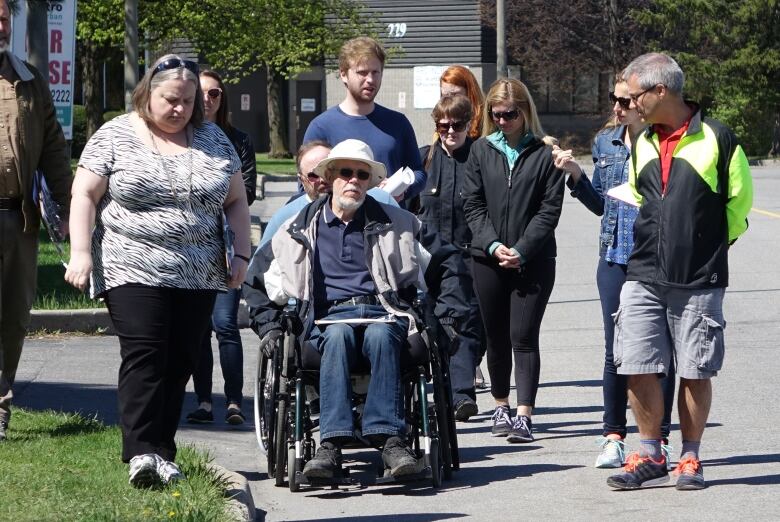 A group of people make their way down a city street. Most are walking and some use wheelchairs.