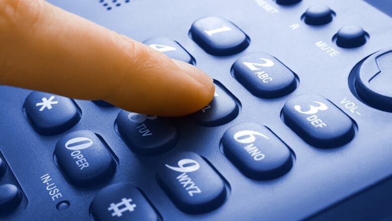 A close up image shows a finger pressing a number on a phone.