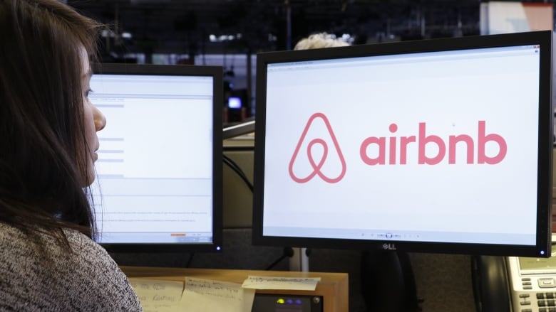 A woman looks at a computer screen with Airbnb logo on it.