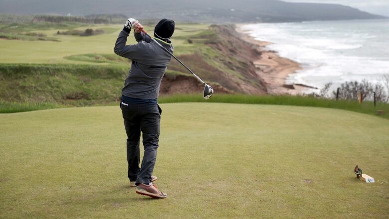 A golfer hits from a tee at a cliffside gold course.