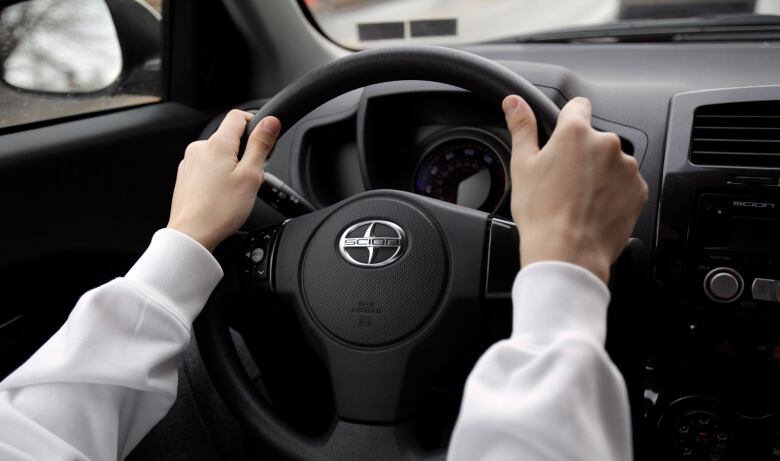 Hands grasp the steering wheel of a car.