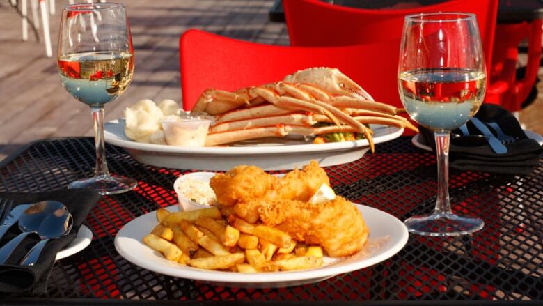 Two plates with seafood and two wine glasses on a restaurant table.