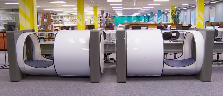 Two white cylindrical sleeping pods pictured side by side inside a college library.