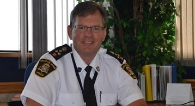 Robert Keetch wears a white police uniform and smiles for the camera, with plants and a window behind him.