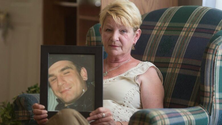 A woman holds up a frame containing a picture of a man to the camera.