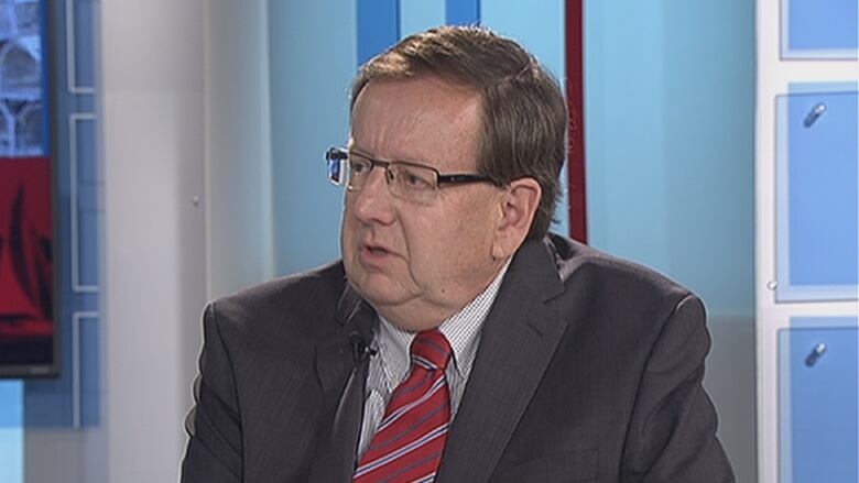 A man in a suit sits in a television studio.