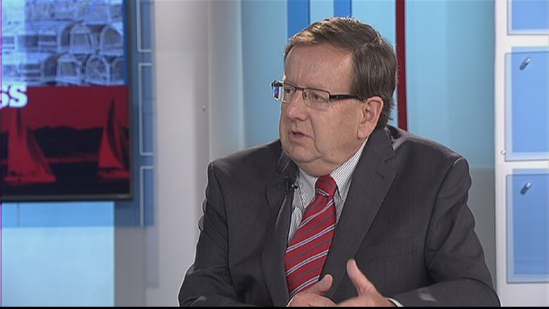 A man in a suit sits in a television studio.