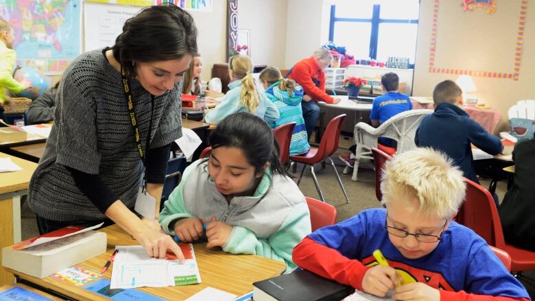 Teacher stands over small group of students in classroom.