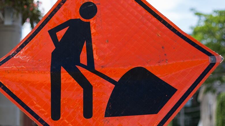 Orange road sign with picture of person shoveling a mount of dirt.