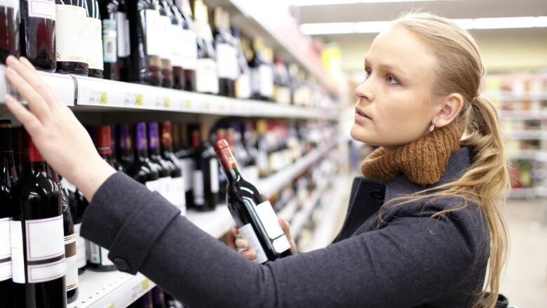 A woman looks at wine bottles sitting on the shelf of a store.