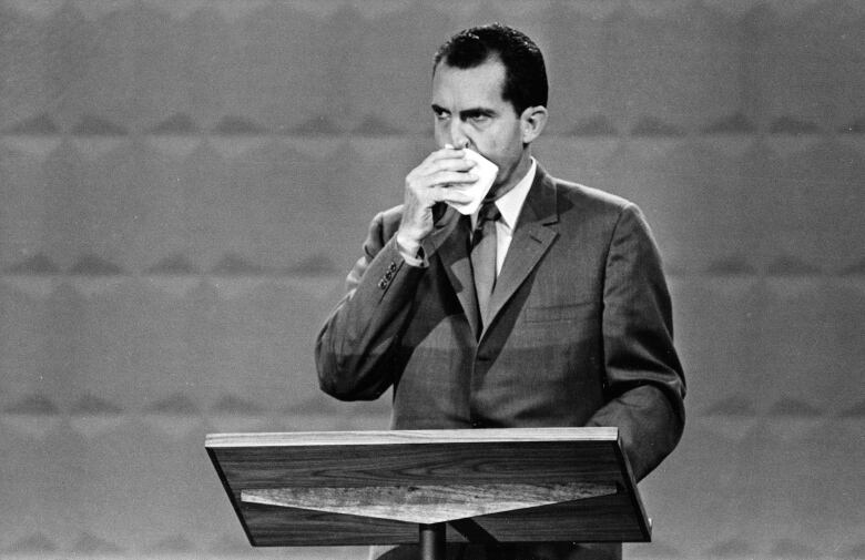 Nixon in black and white photo, seen wiping his face during a debate