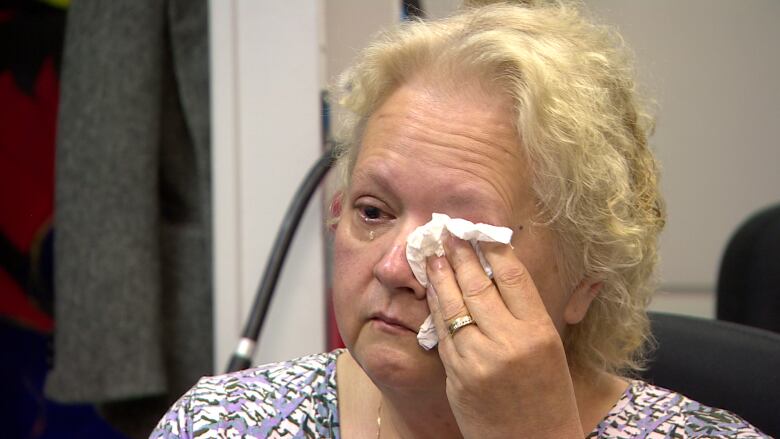 A woman cries and covers her eye with a tissue.