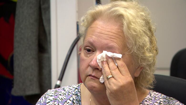 A woman cries and covers her eye with a tissue.