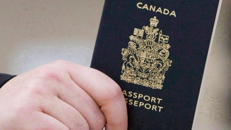 A close-up photo shows a hand holding a Canadian passport. 