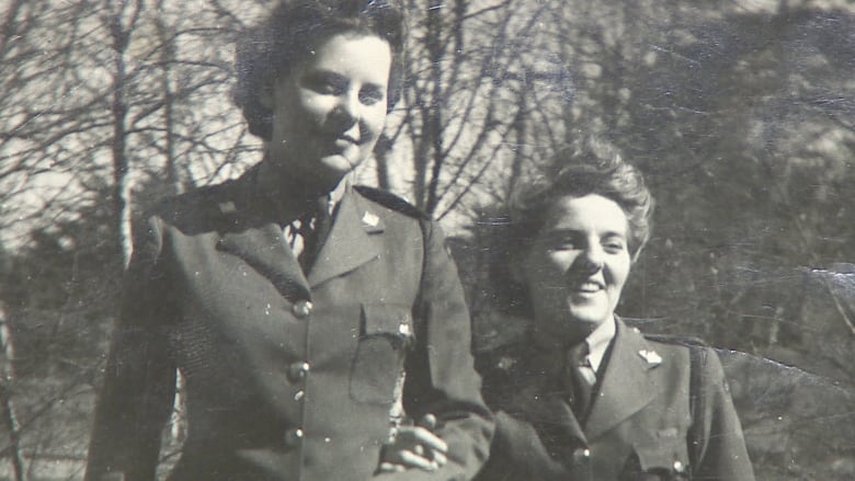 Black and white photo of two women walking arm in arm in military uniforms.