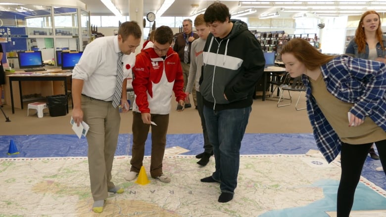 People stand on a map spread out on a floor.