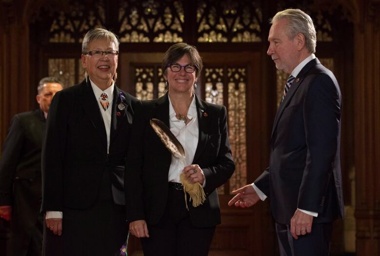 A woman stand holding an eagle feather flanked by a colleage on each side.