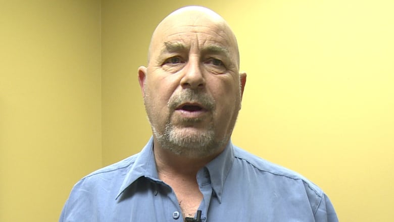 A close up of a middle-aged bald man wearing a blue button-up shirt.