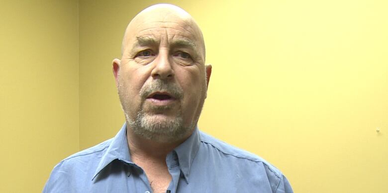 A close up of a middle-aged bald man wearing a blue button-up shirt.