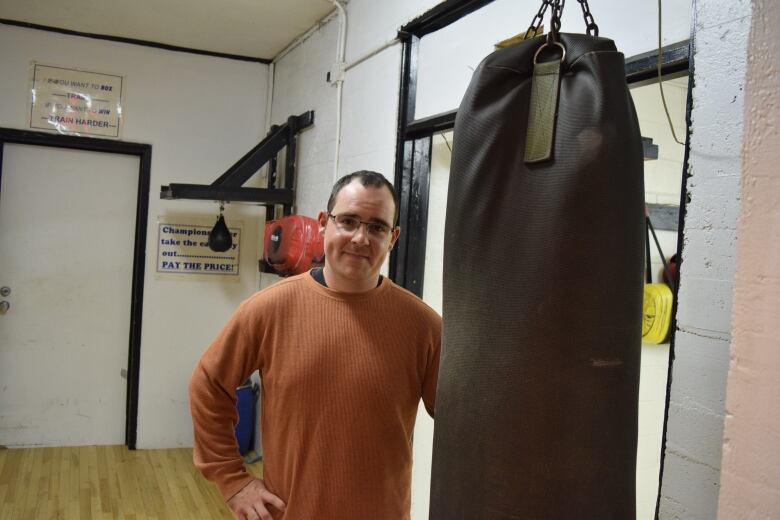 A man stands next to a boxing bag in a gym.