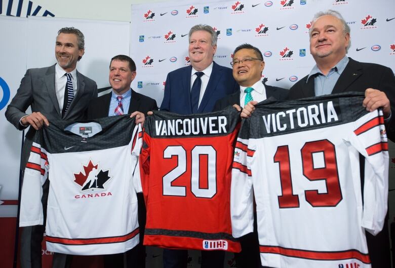 Five men are pictured standing holding up sports jerseys. 