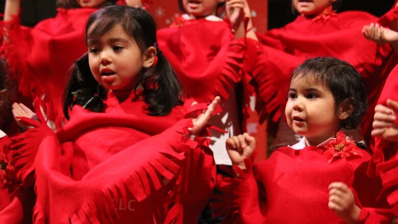 Young girls in red shawls sing as part of a choir