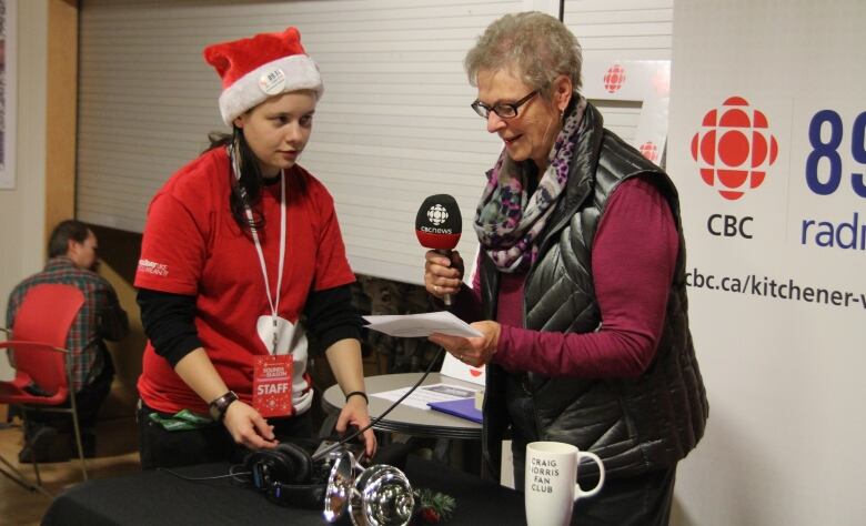 A woman holds a microphone to record while a volunteer stands by