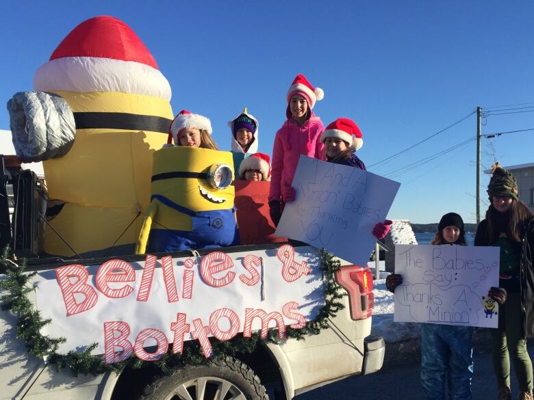 Several children wearing Santa hats ride in a truck that says 