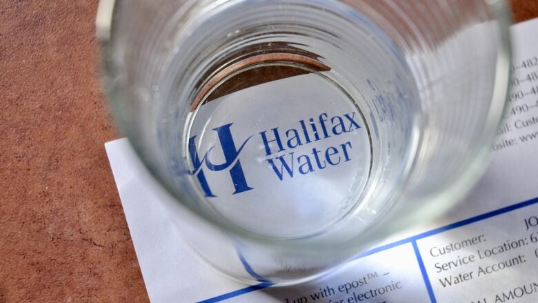 The logo of Halifax Water on a bill is seen through a glass of water.