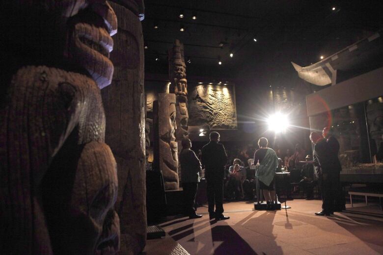 People stand on a stage among totem poles